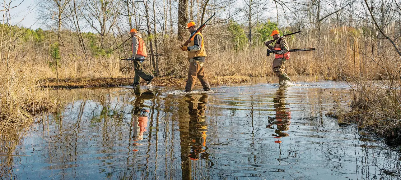 three hunters walking through swamp