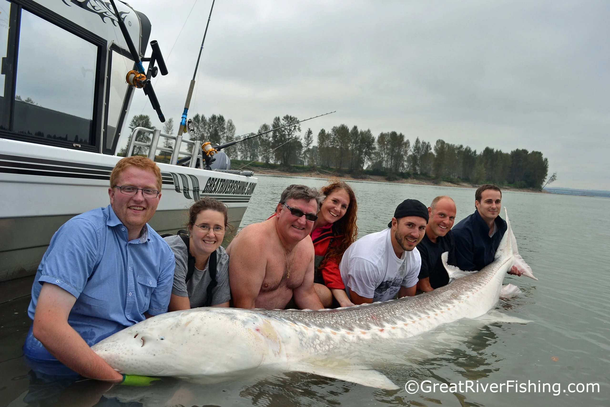 people pose in water with white sturgeon