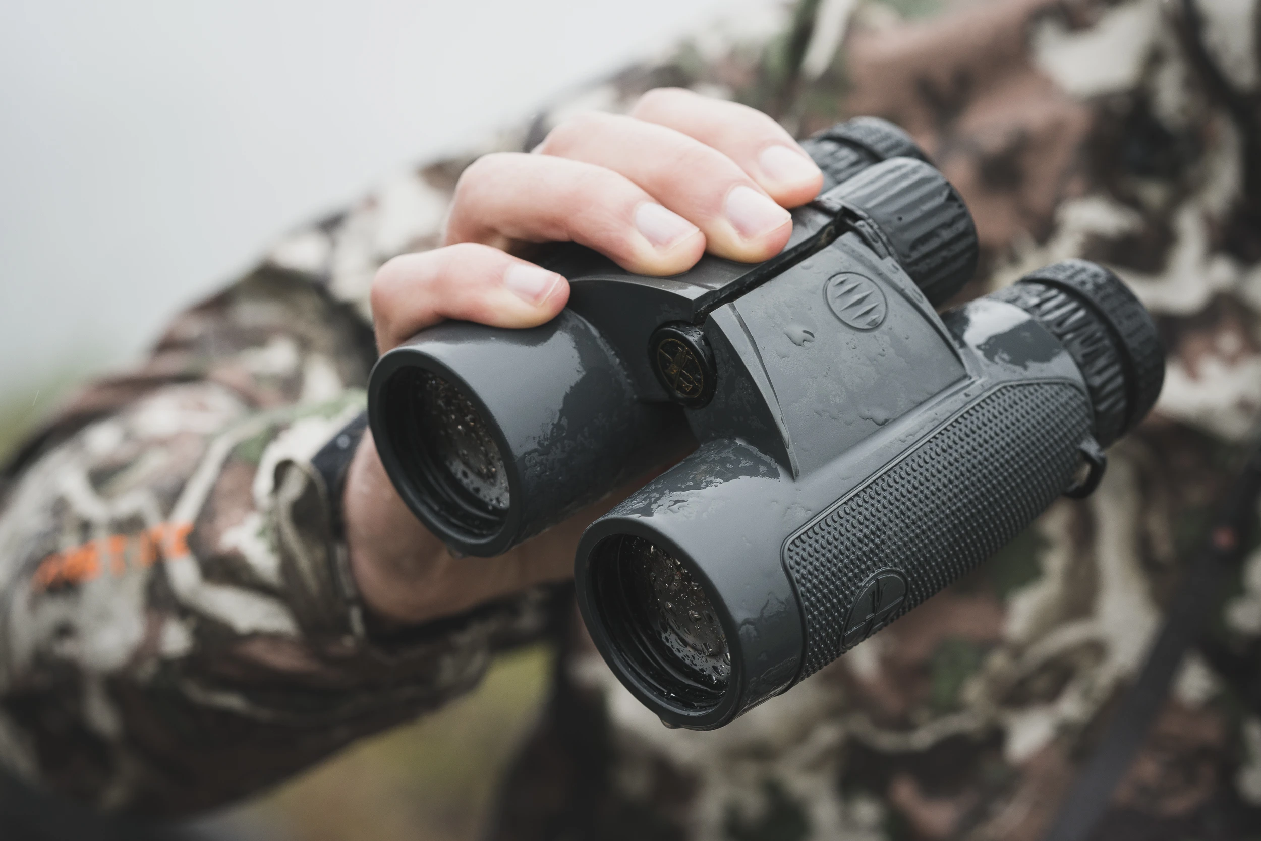 A man holds the Leupold BX-4 Range HD binocular in one hand, his camo shirt in the background. 