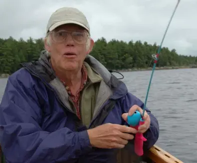 A man in fishing gear holds up a kids fishing pole.