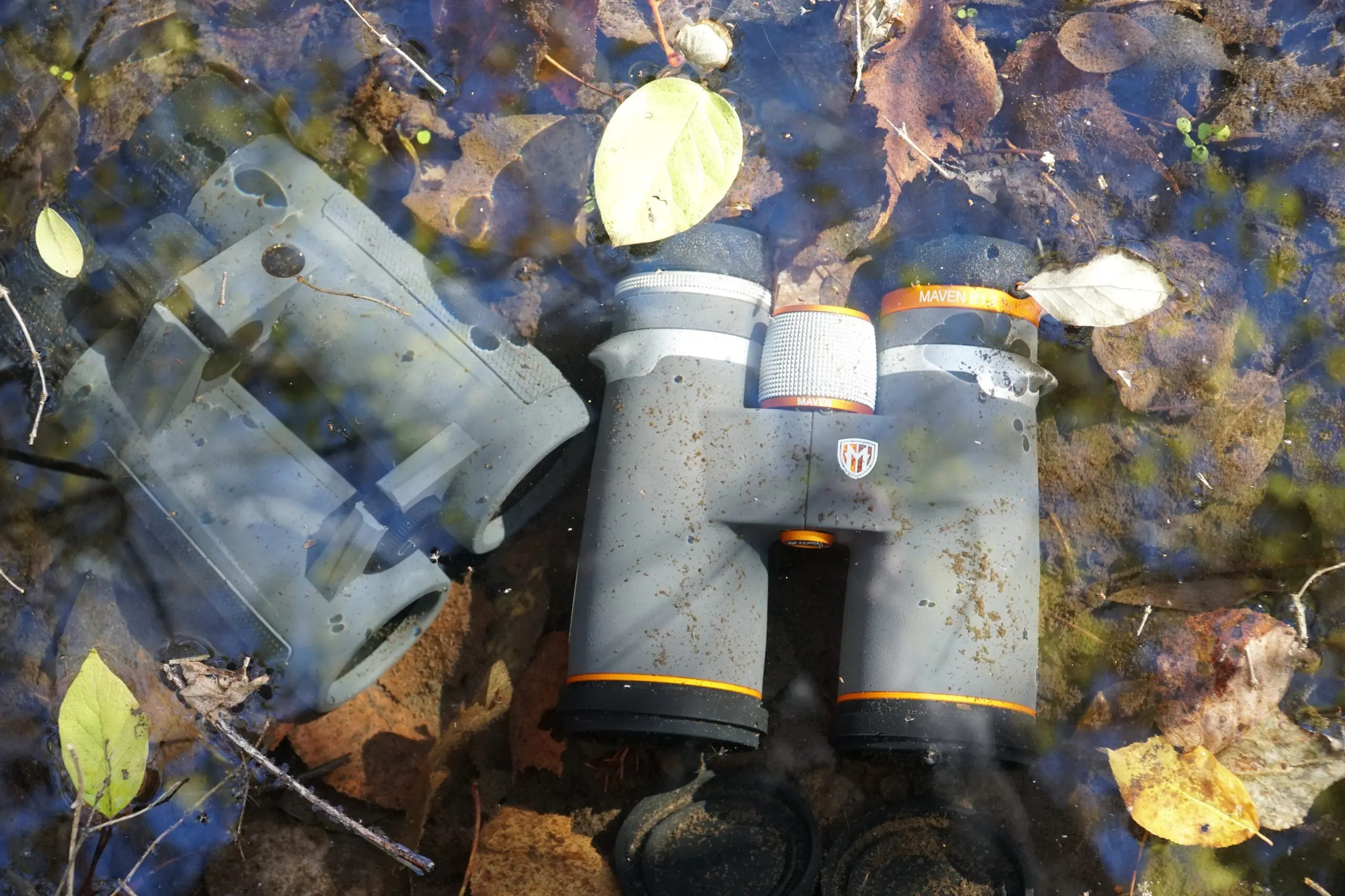 Two binoculars underwater in a creek with fall leaves.