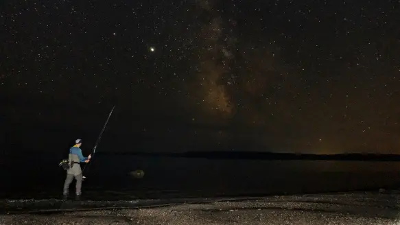 Striped bass angler fishing the shore under a full moon.