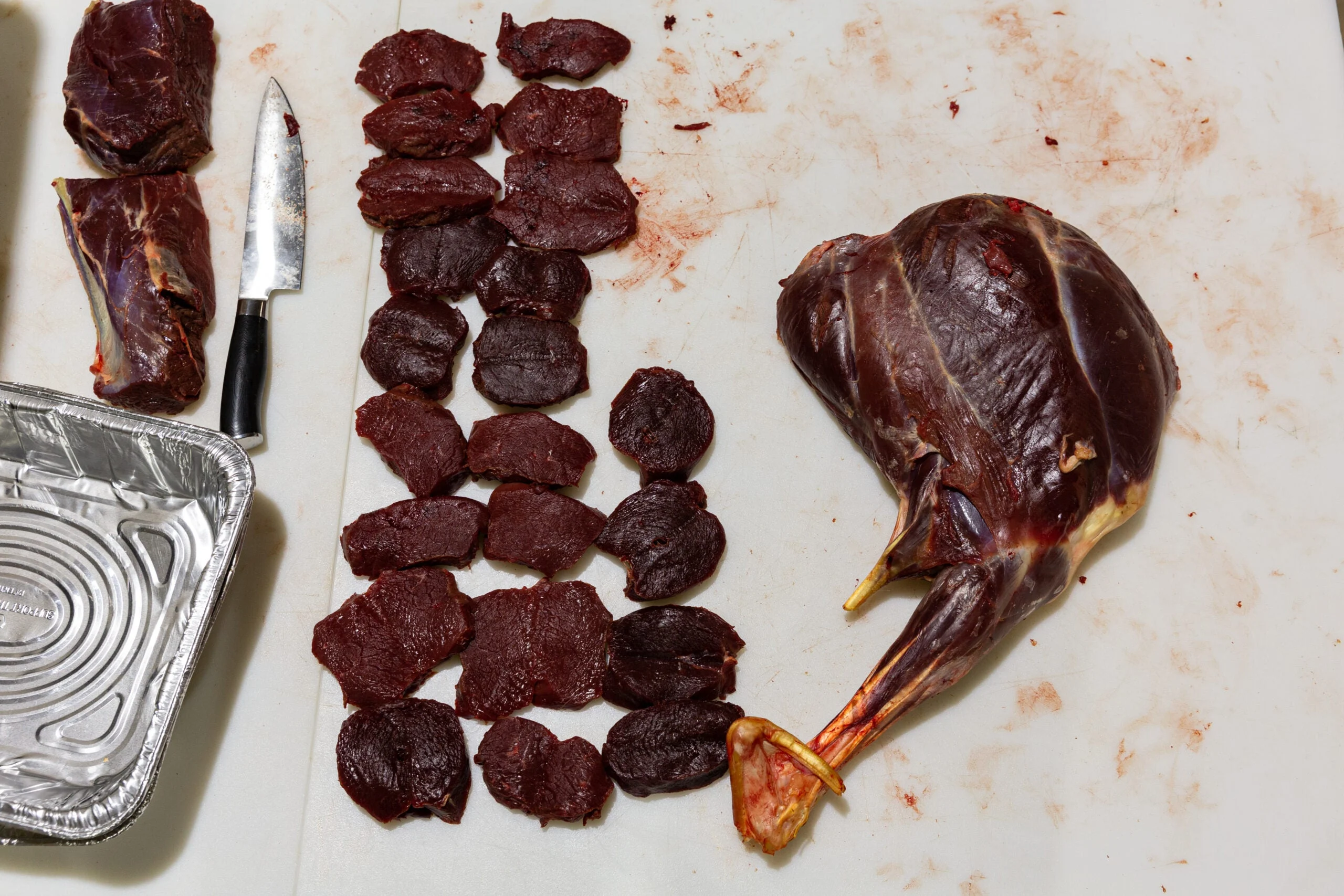 An assortment of venison cuts from a whitetail deer on a white cutting board.