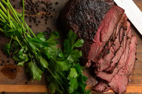 A whitetail deer venison roast on a cutting board with a bunch of green parsley.