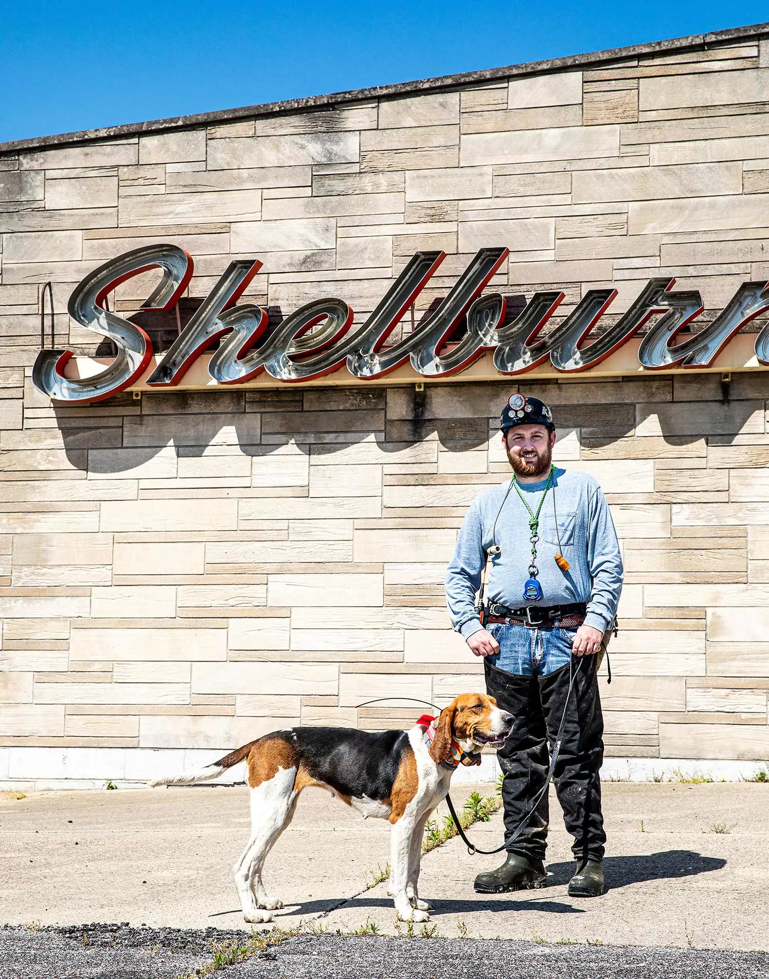 Josh Sizemore and Bella pose in front of a stone wall with a sign reading Shelburn