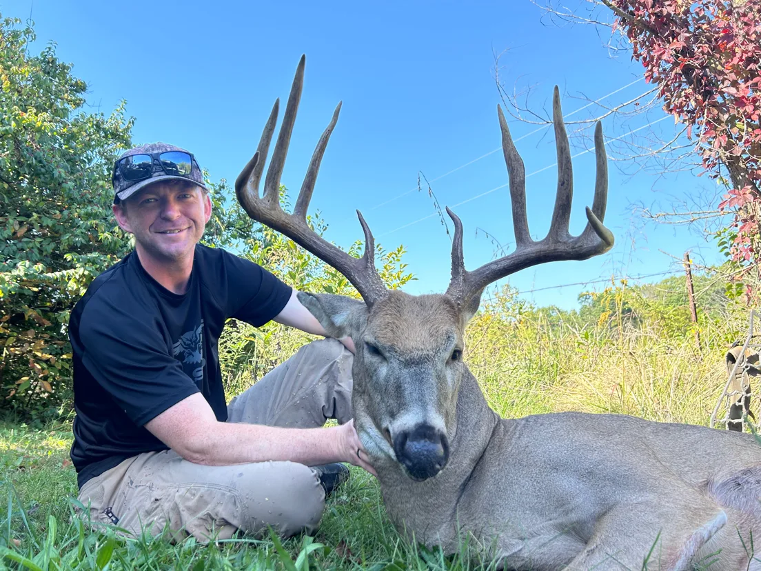 Hunter Jace Allen sits on the ground in a field and shows off a big Missouri whitetail he took with a bow. 