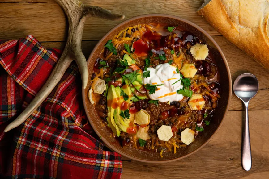 A bowl of venison chili with avocado and sour cream on a table.