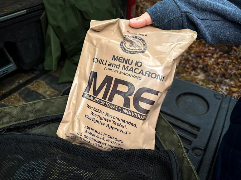 A hiker reaches for an MRE bag on a outdoor trip