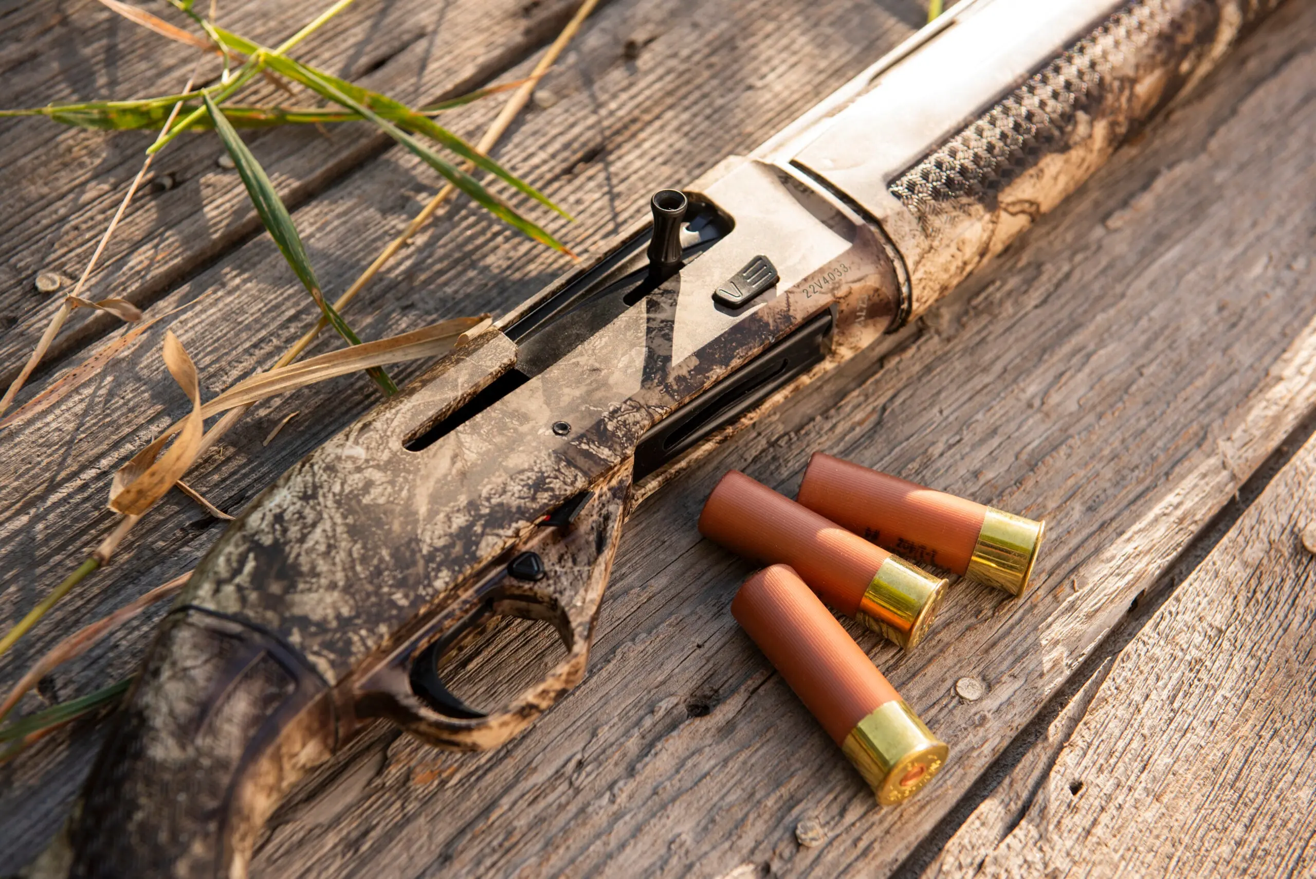 Close-up of the new CZ 712 G3 shotgun lying on an old barn door, with marsh grass and two shells nearby.