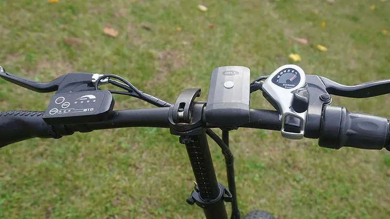 The handlebars and controls of an Ecotric fat tire bike against a green grass background. 