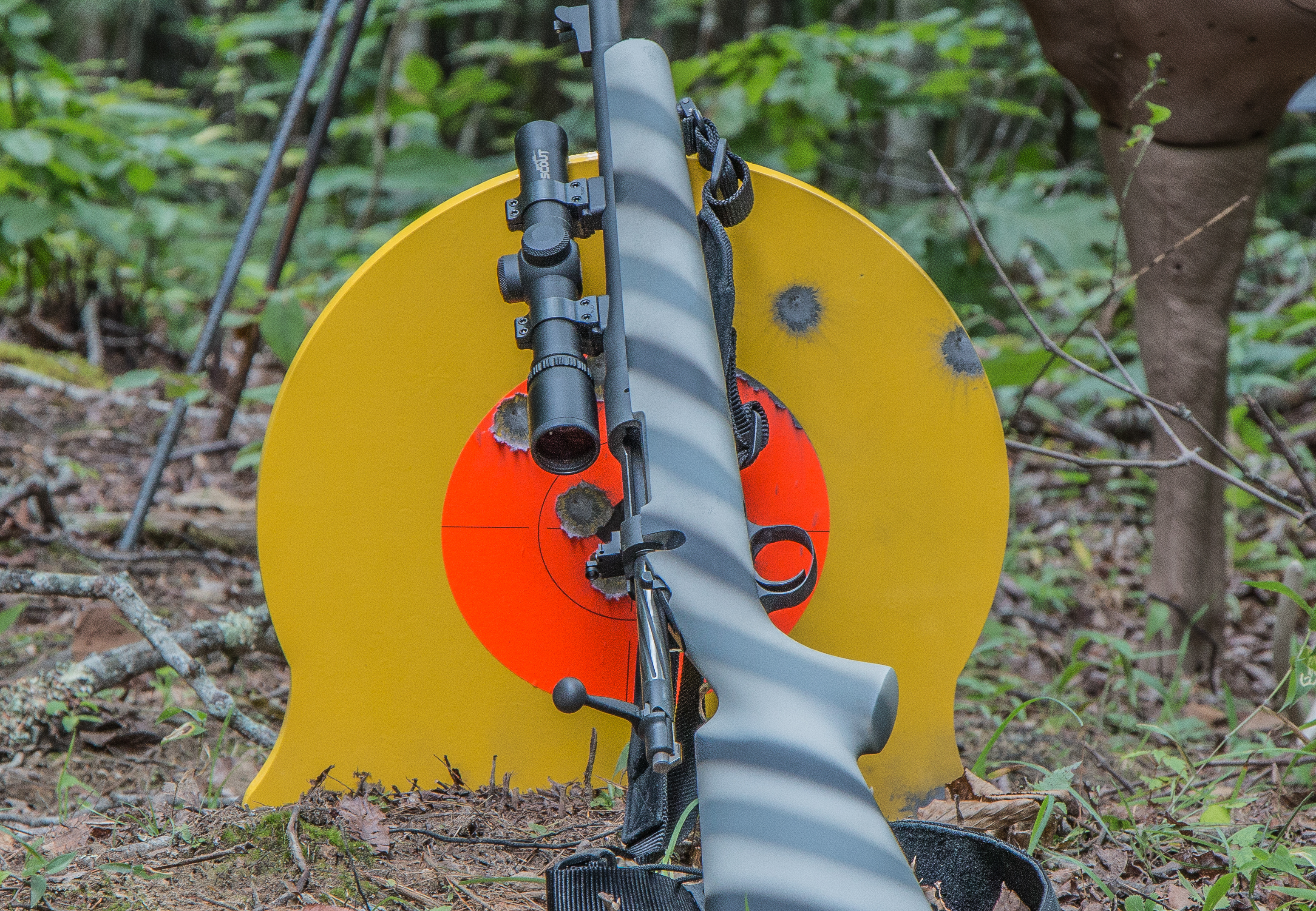 A rifle rests against a steel target with several bullet splash marks in it. 