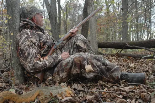 Hunter sitting against a tree with a black powder long rifle.