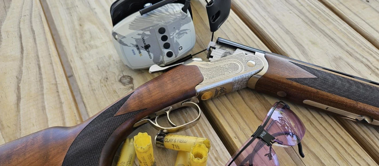 Mossberg's new 20-gauge Gold Reserve over-under shotgun on a wood surface with hearing protection, shooting glasses, and empty hulls.