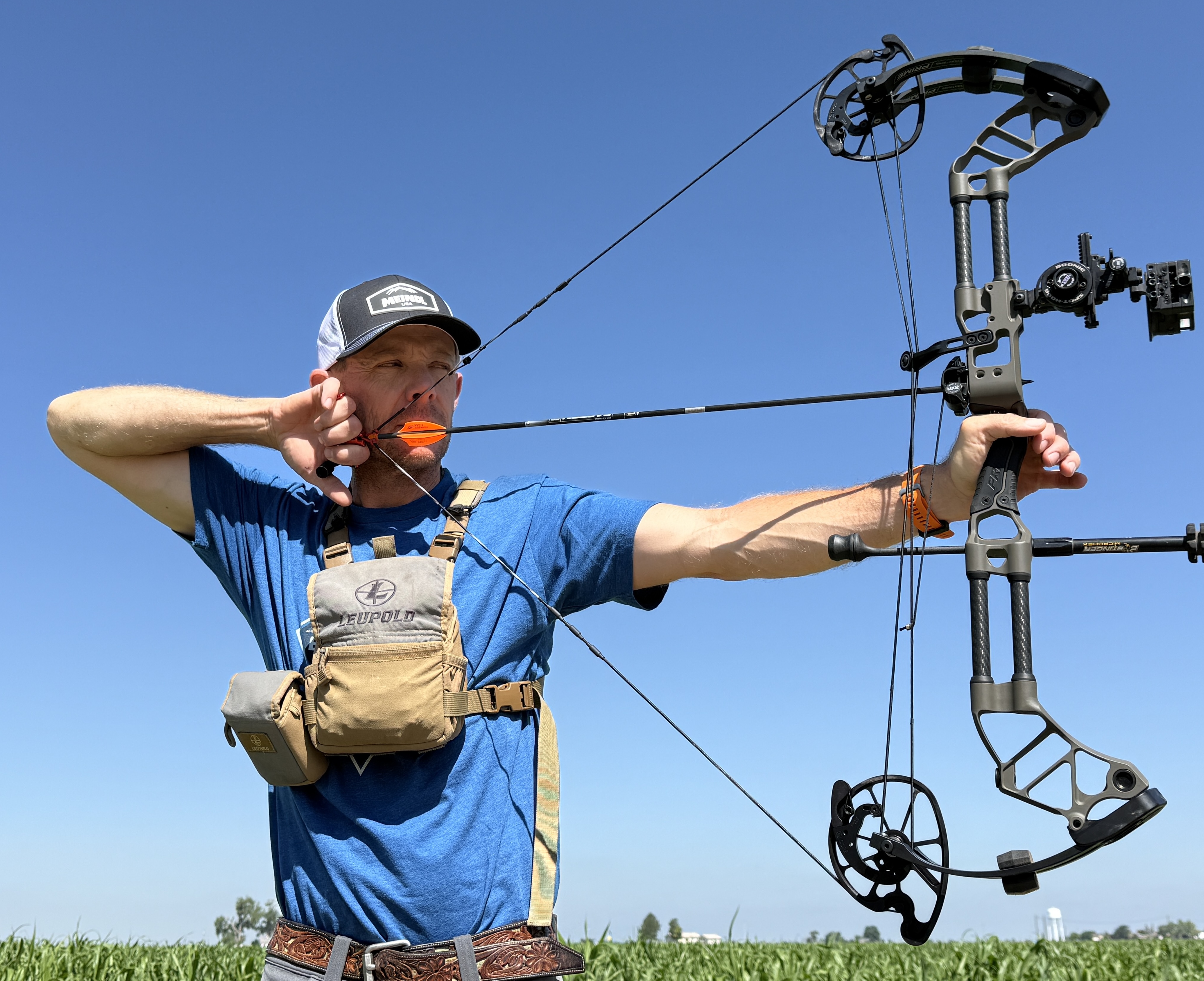 An archer shoots a compound bow with blue sky in the background. 