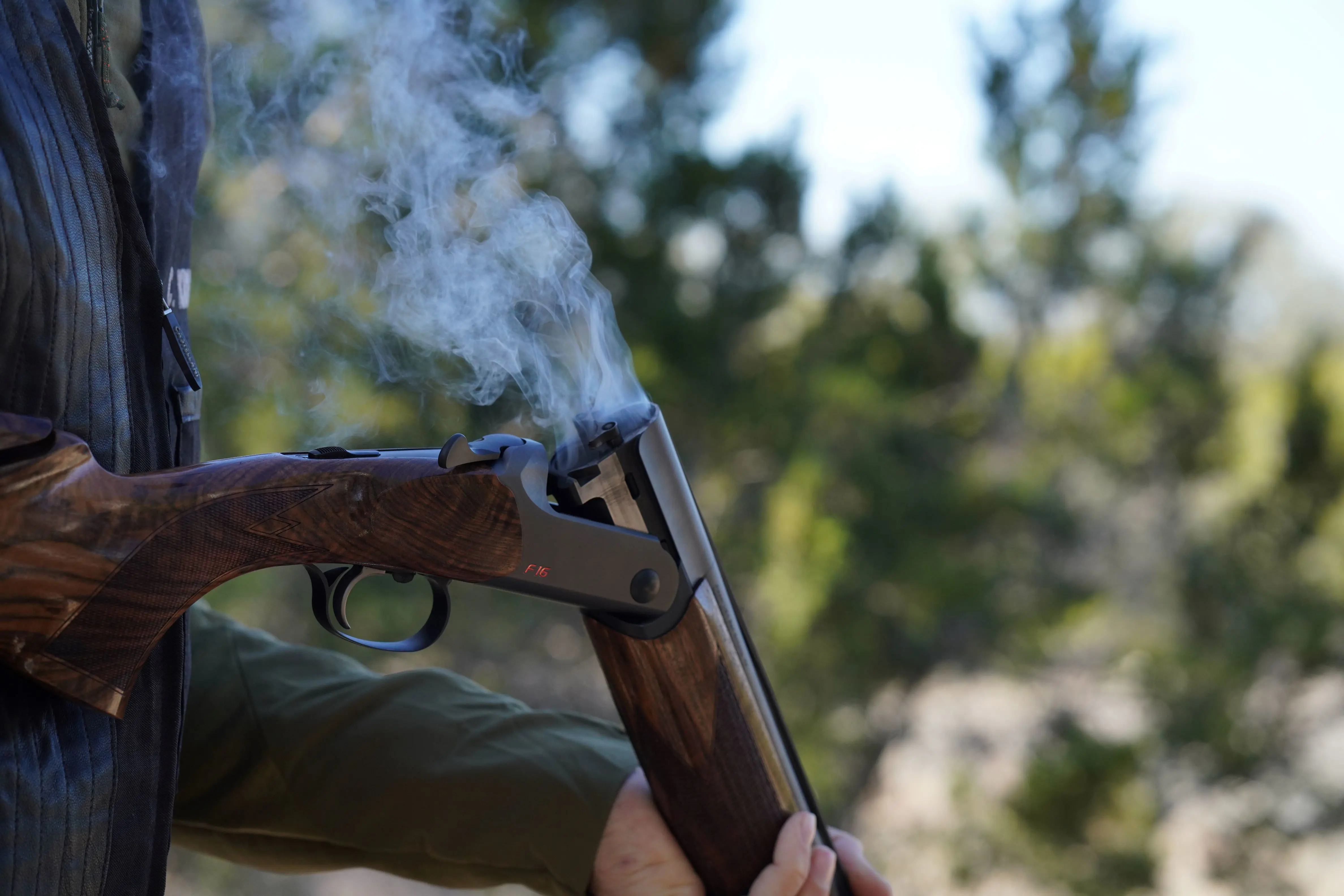 Hunter ejects shell from Blaser F16 Pro Sporting shotgun as smoke rises out of the barrels.