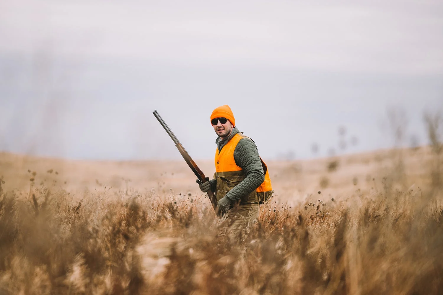 Bird hunter in orange hat and vest stands in field.