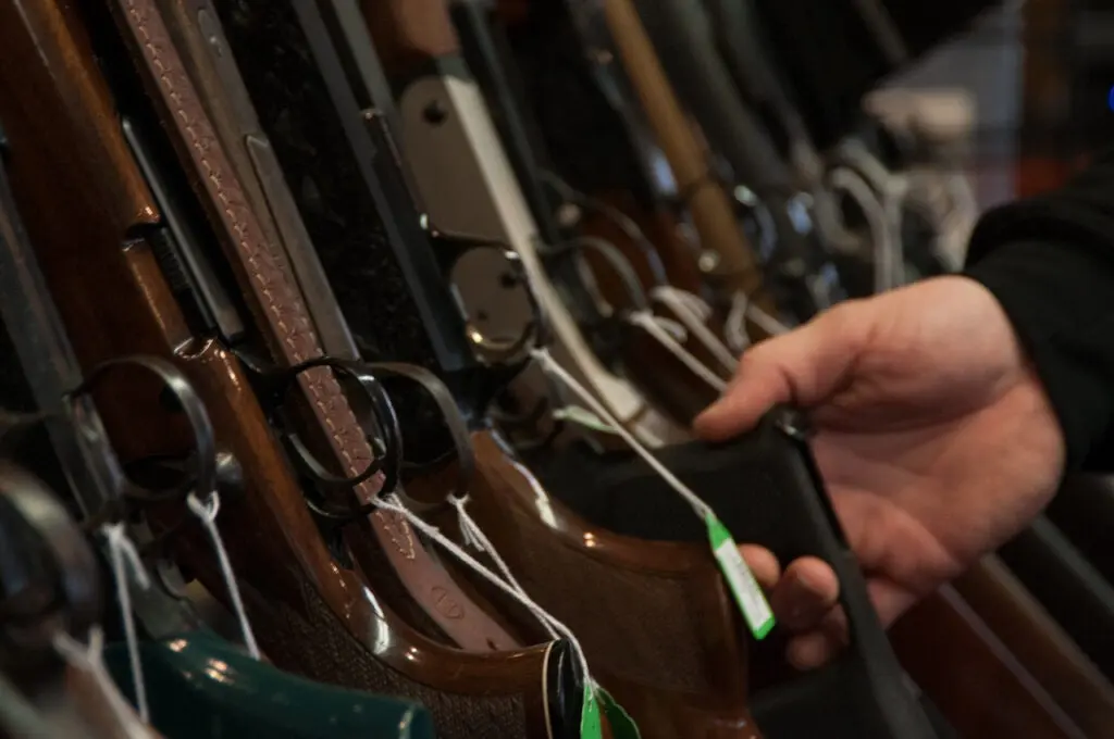 Hand picking out a gun for sale on the rack at a gun store.