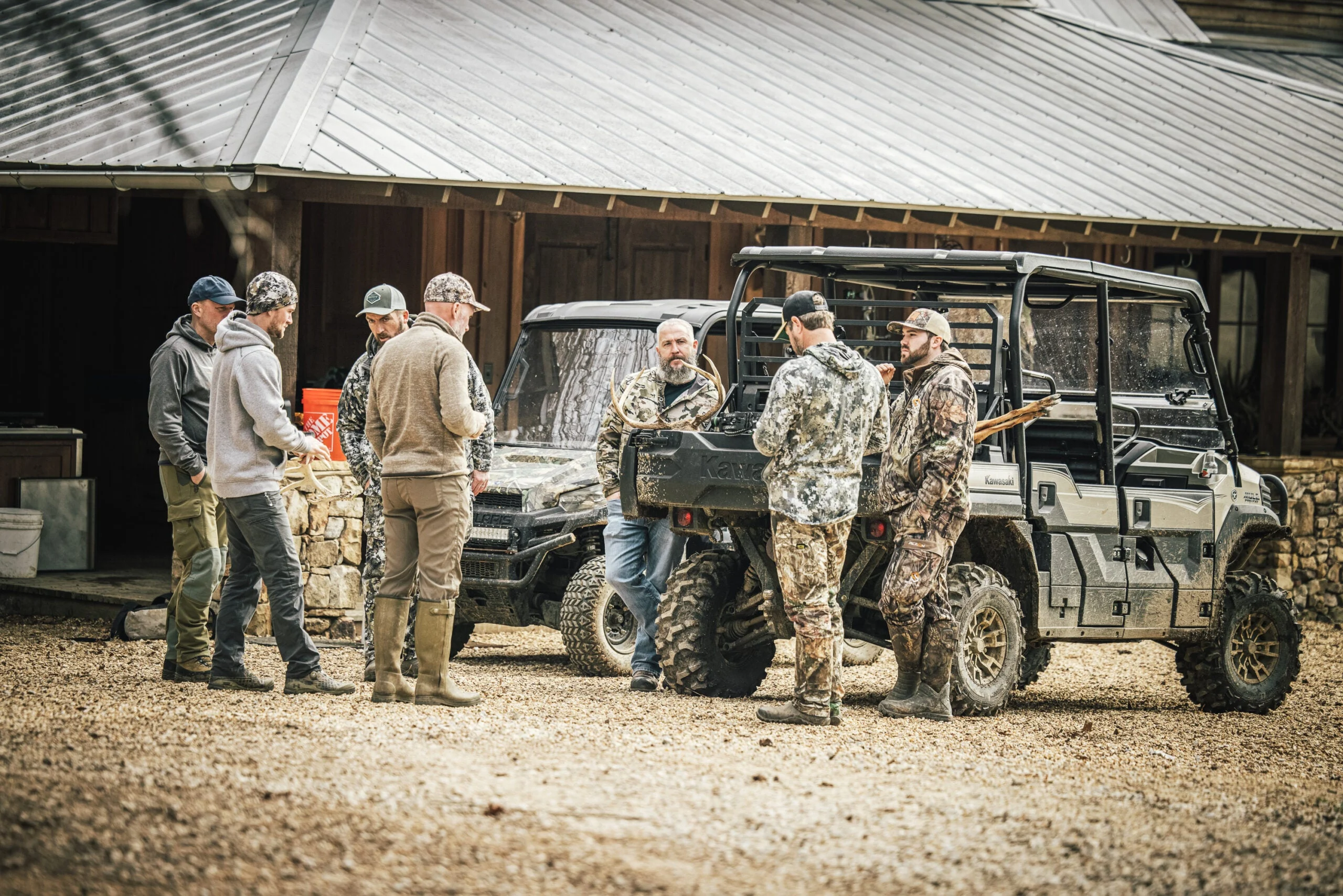 A group of hunters at a deer camp gather around a ATV hauling a whitetail buck.