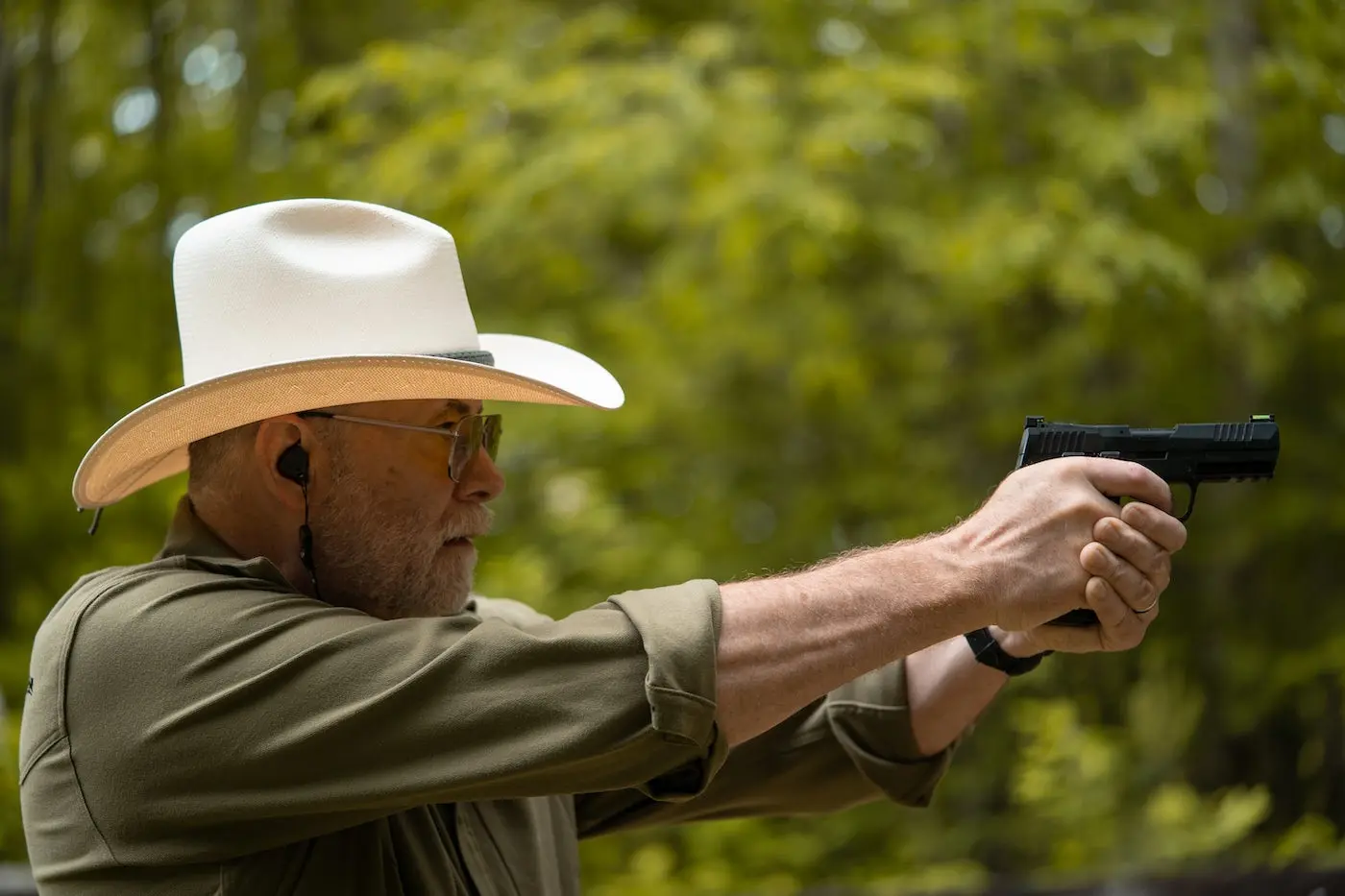 Man in a cowboy hat shooting a handgun.