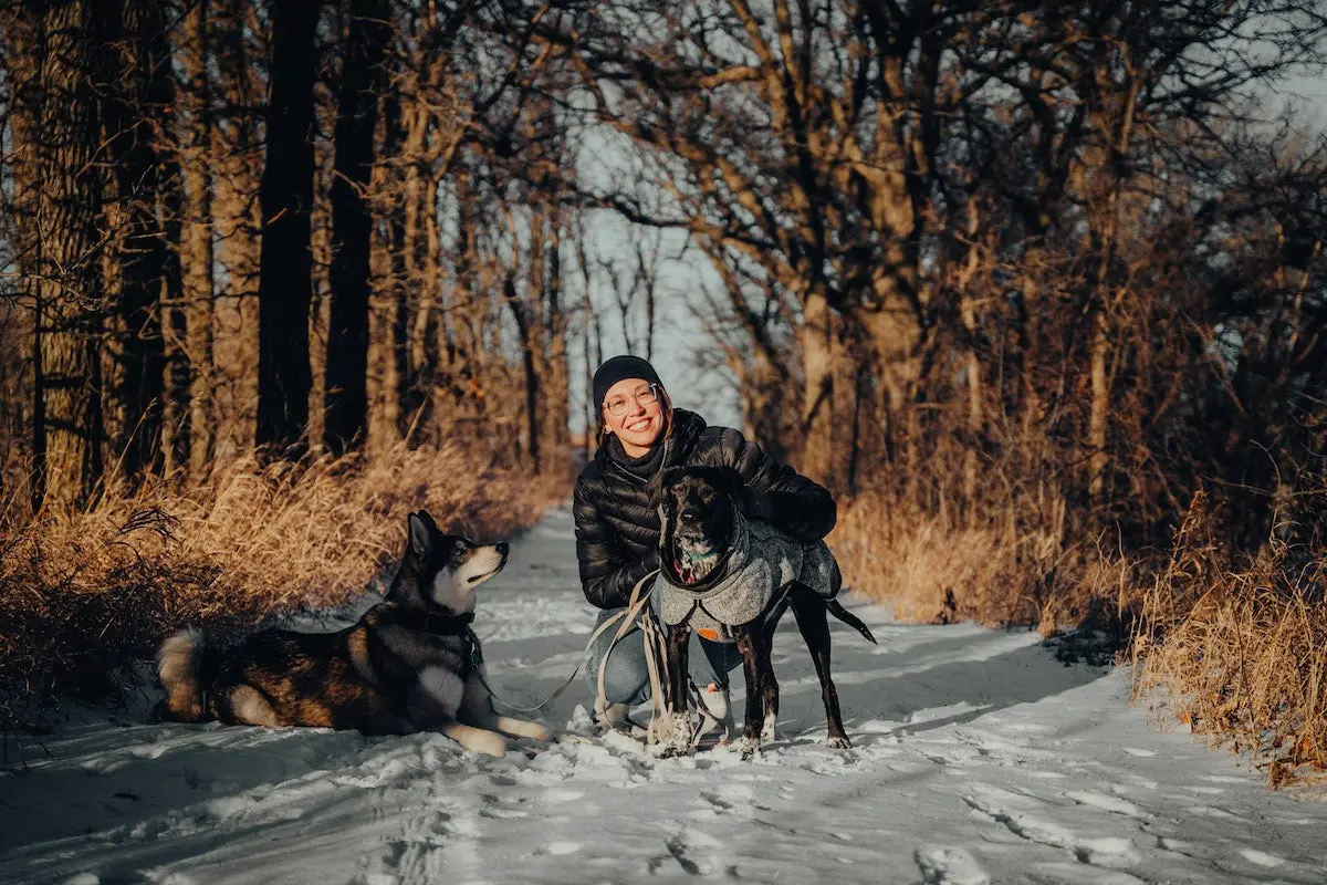 Female hiker wearing Nathan puffer jacket in the snow with dogs