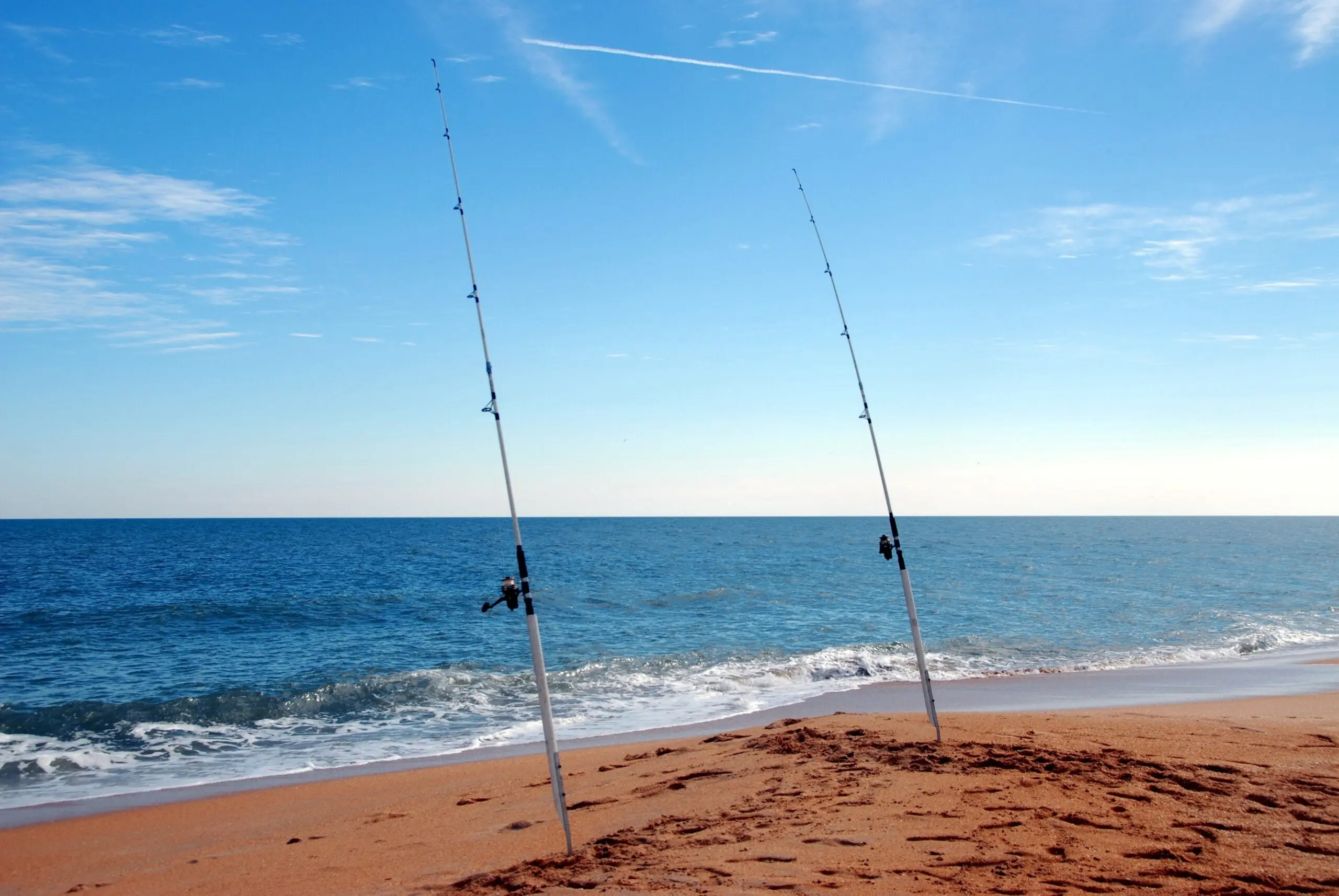 Surf casting rods sit in PVC sand spikes on a beach.