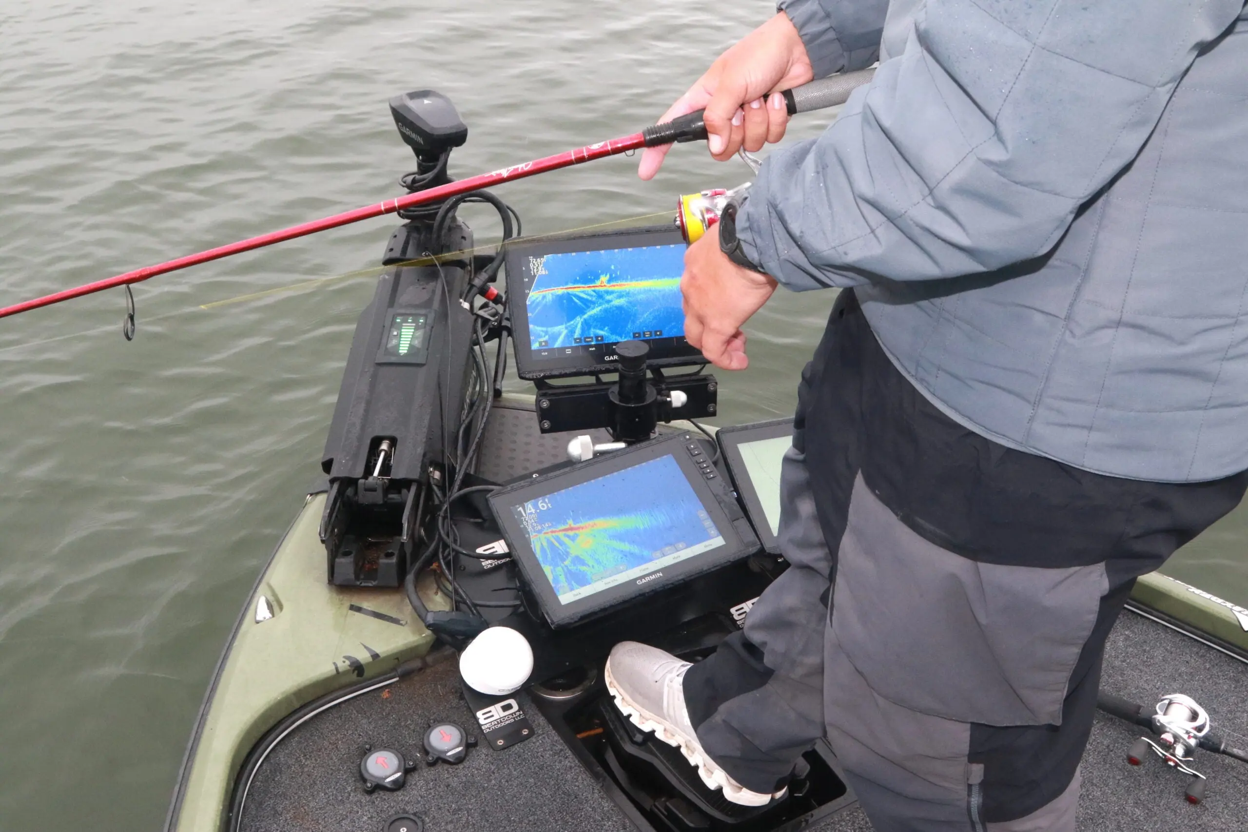 And angler on a lake in a bass boat with a panel of electronic fishfinders at his feet.