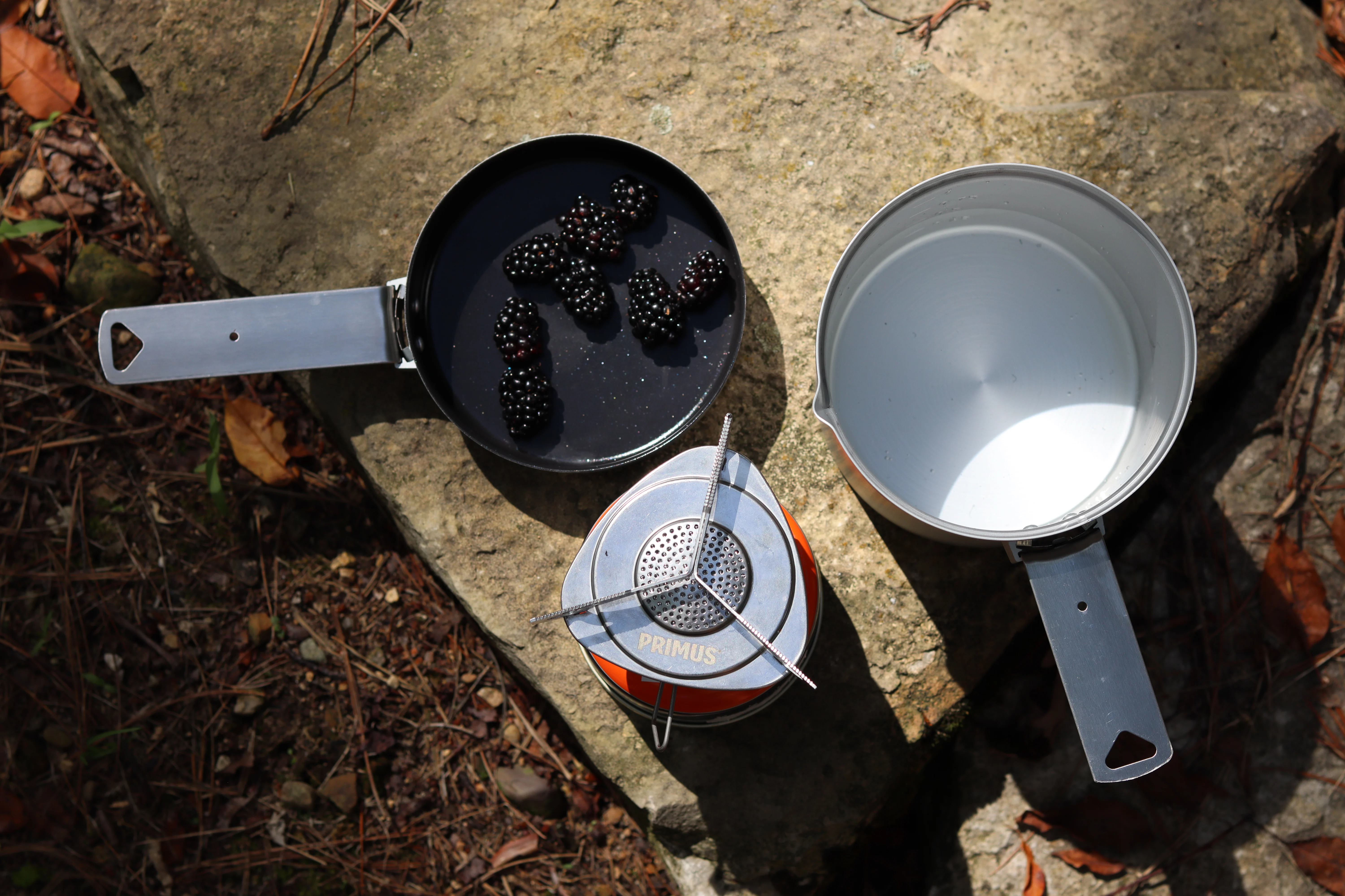 A pot, pan, and jetboil stove sitting on a rock in the backcountry