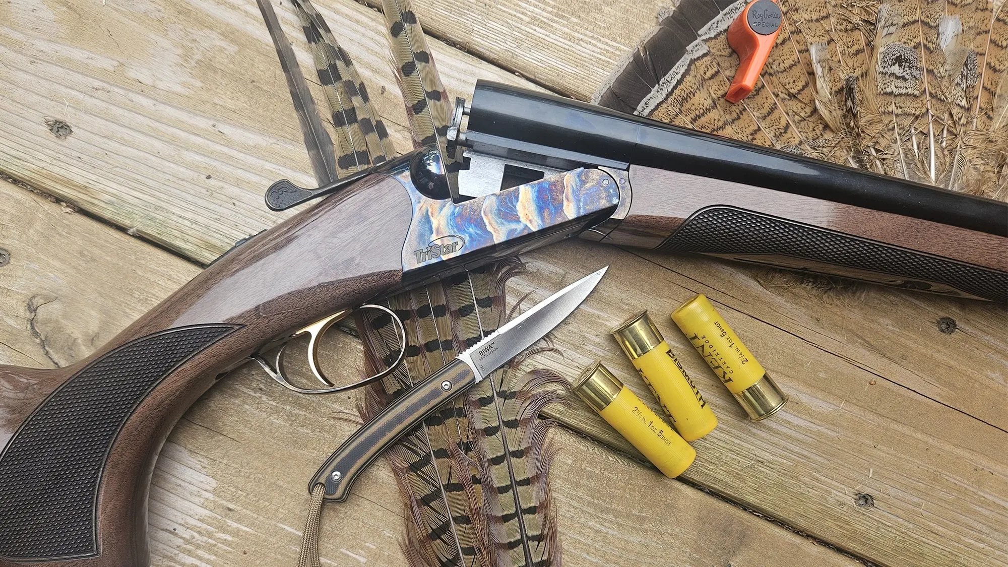 Tristar Phoenix side-by-side shotgun on a wood surface with feathers, shells, and a knife.