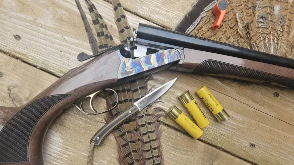 Tristar Phoenix side-by-side shotgun on a wood surface with feathers, shells, and a knife.