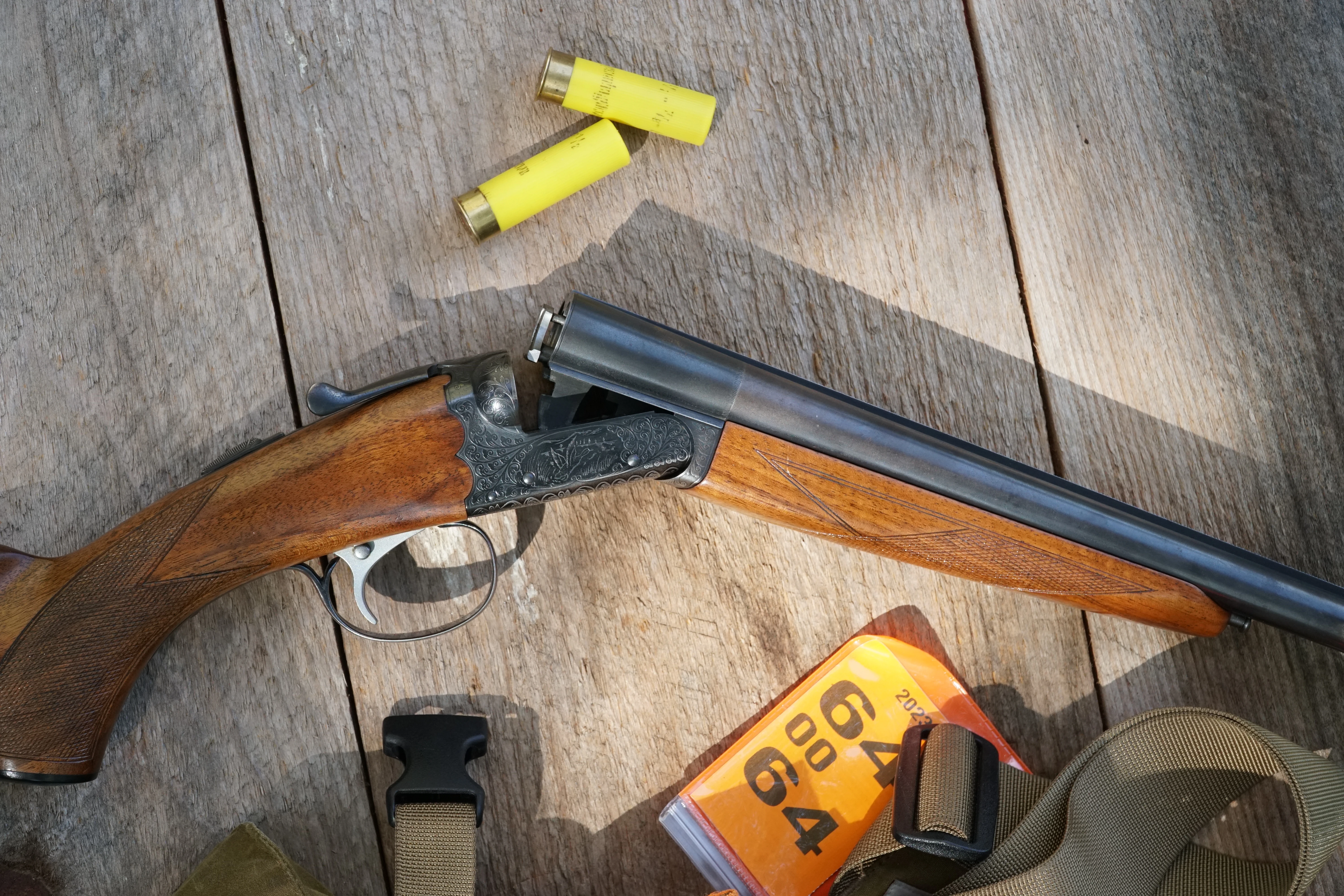 An SKB Model 100 side-by-side shotgun on a table with shells and vest. 