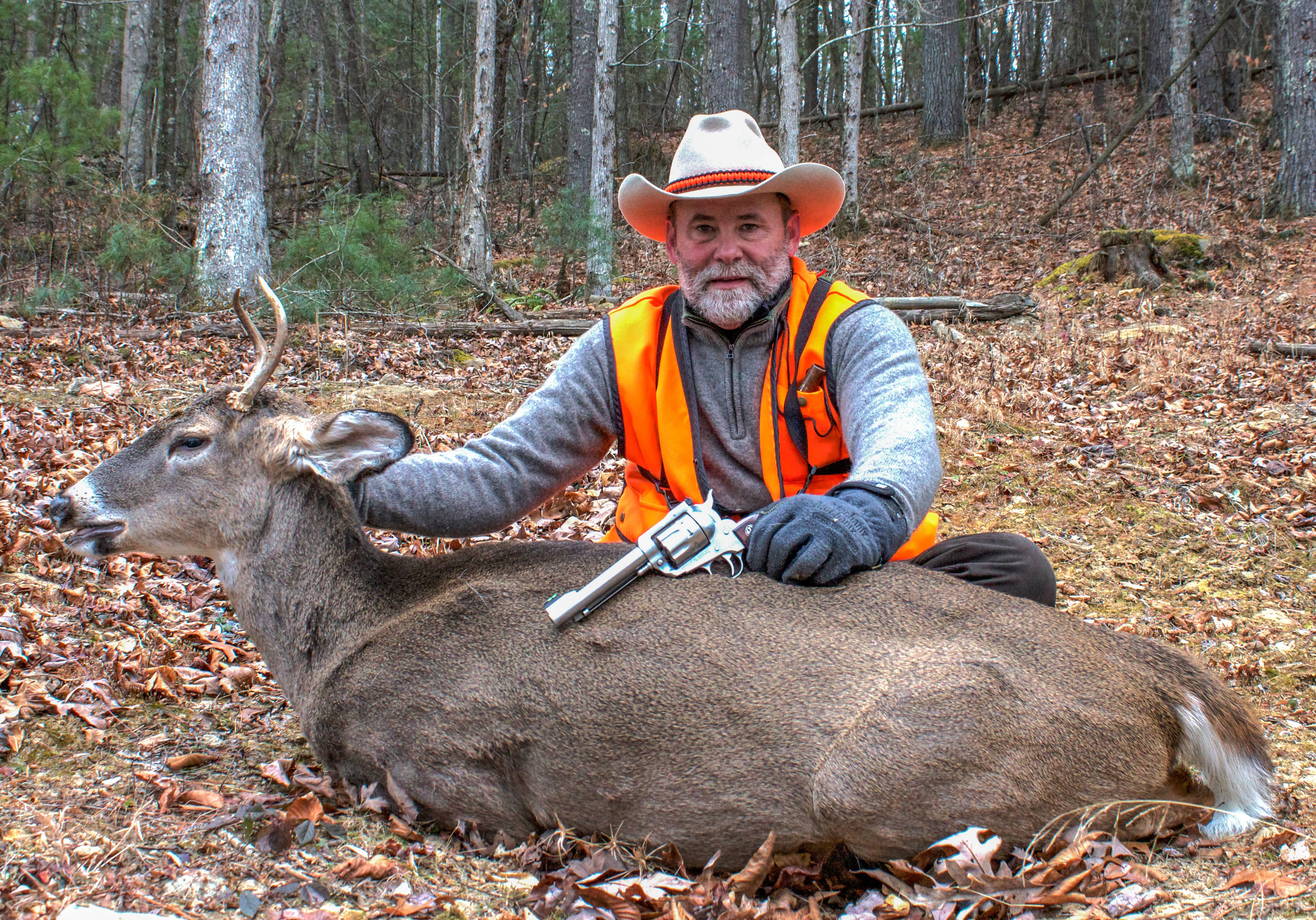 A hunter poses with a whitetail deer taken with a handgun.