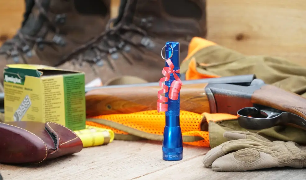 A Mini Maglight with red ribbon among upland hunting gear