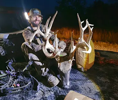 Kansas hunter sitting in the bed of a truck, posing with a huge whitetail buck. 