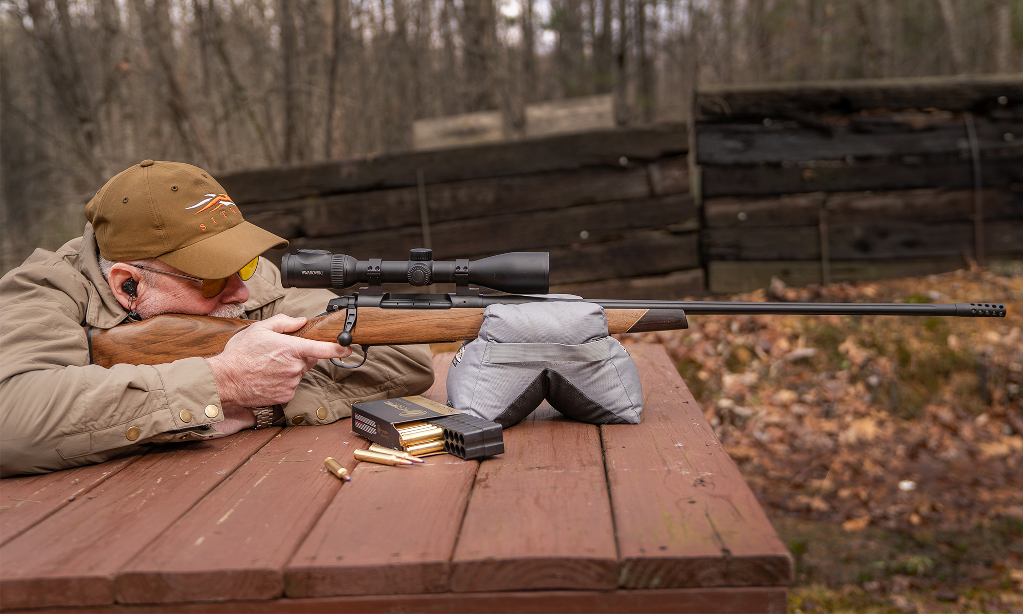 A shooter fires a rifle from a bench rest. 