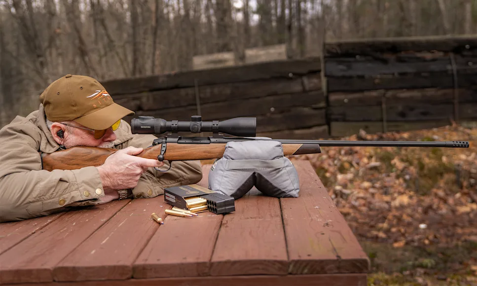 A shooter fires a rifle from a bench rest.