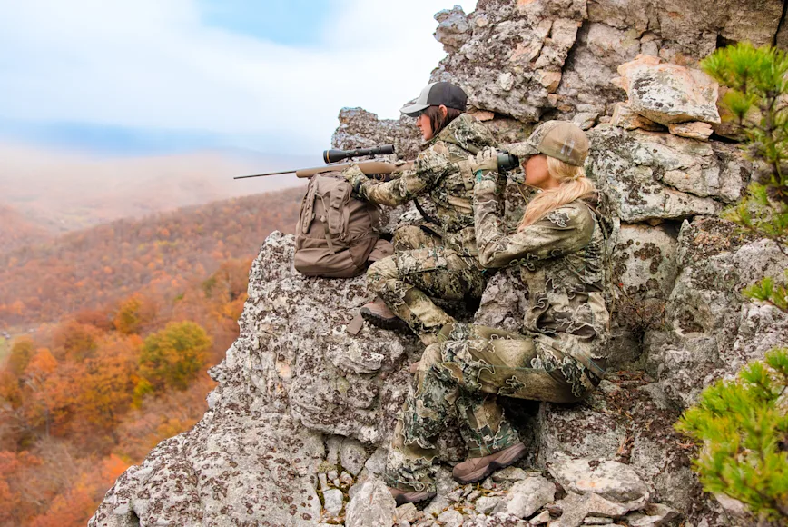 Female hunters sitting on rock ledge with scope