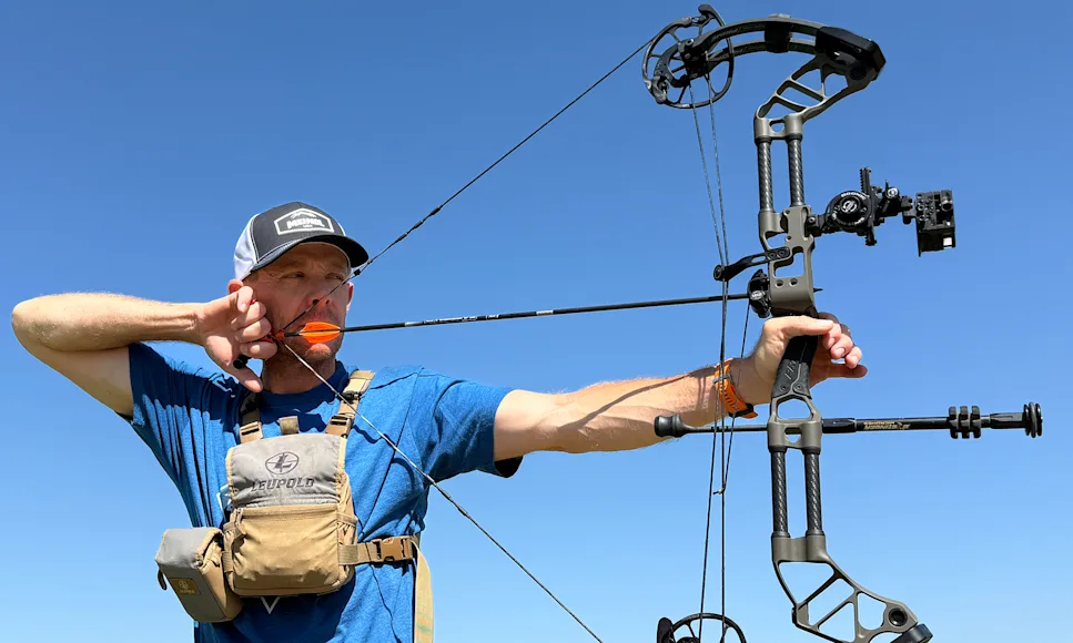 An archer shoots a compound bow with blue sky in the background.