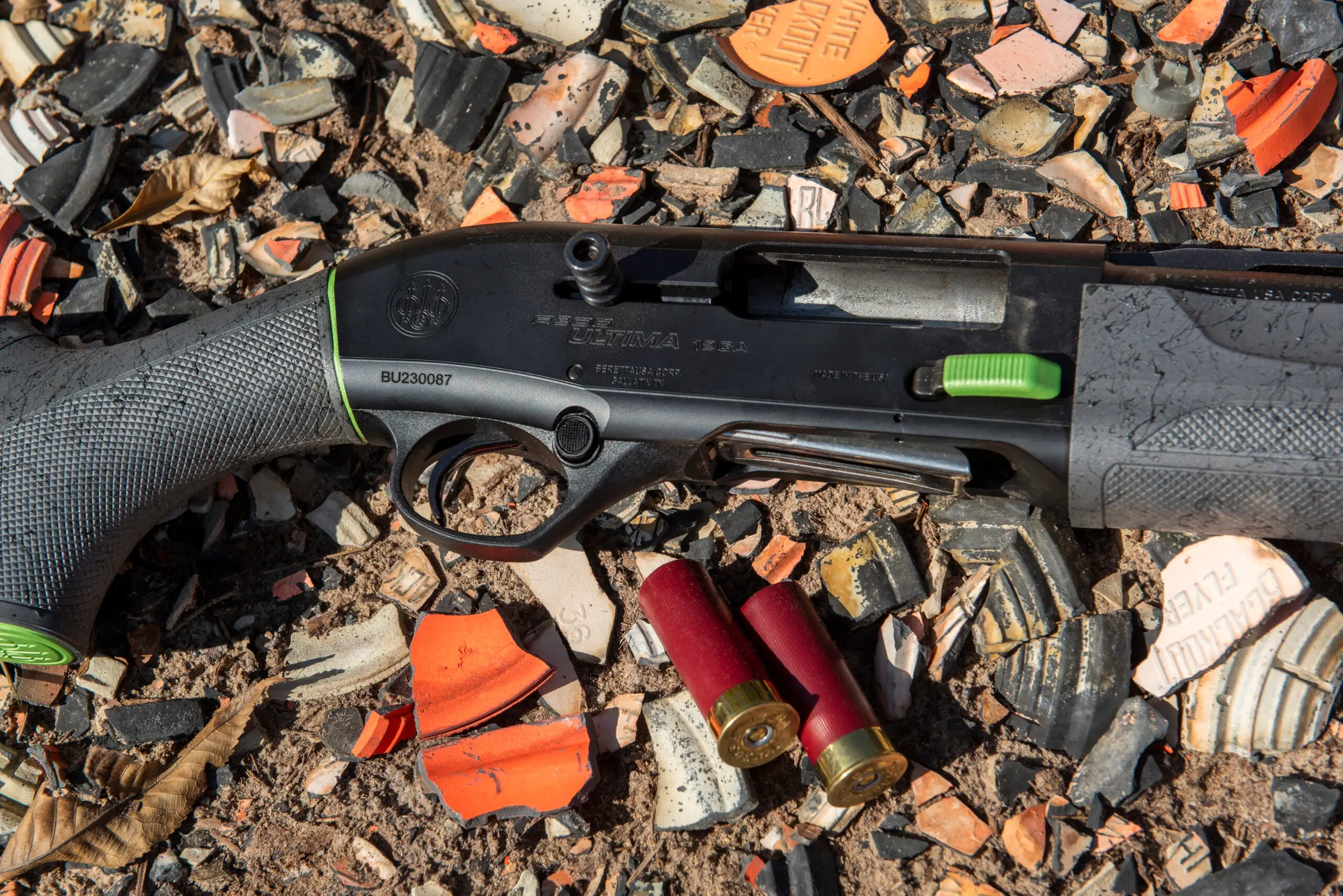 Beretta A300 Ultima Sporting shotgun among broken clay targets, with two shotgun shells nearby.