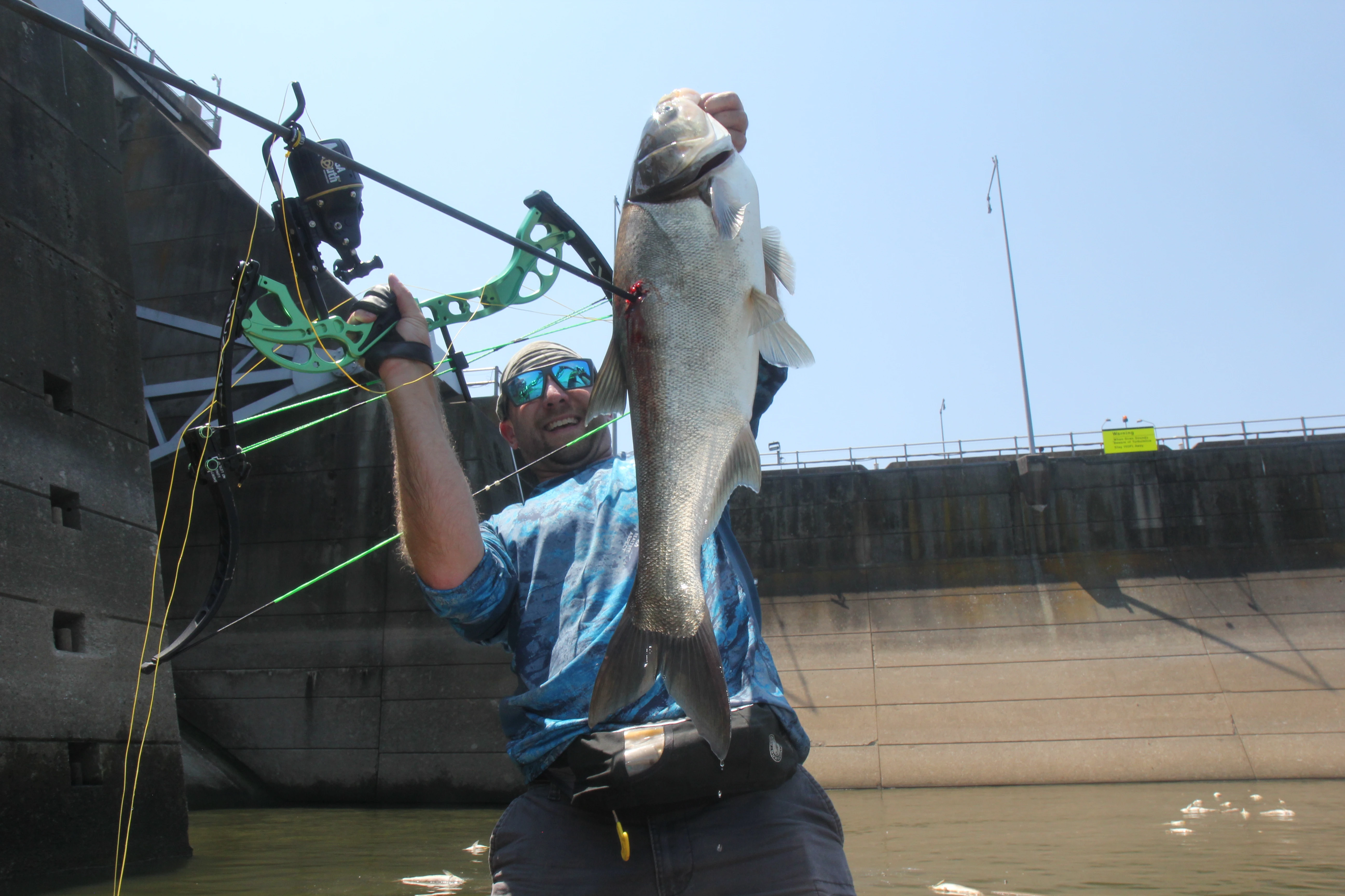 Bowfisherman holds up carp in one hand and an arrow in the other