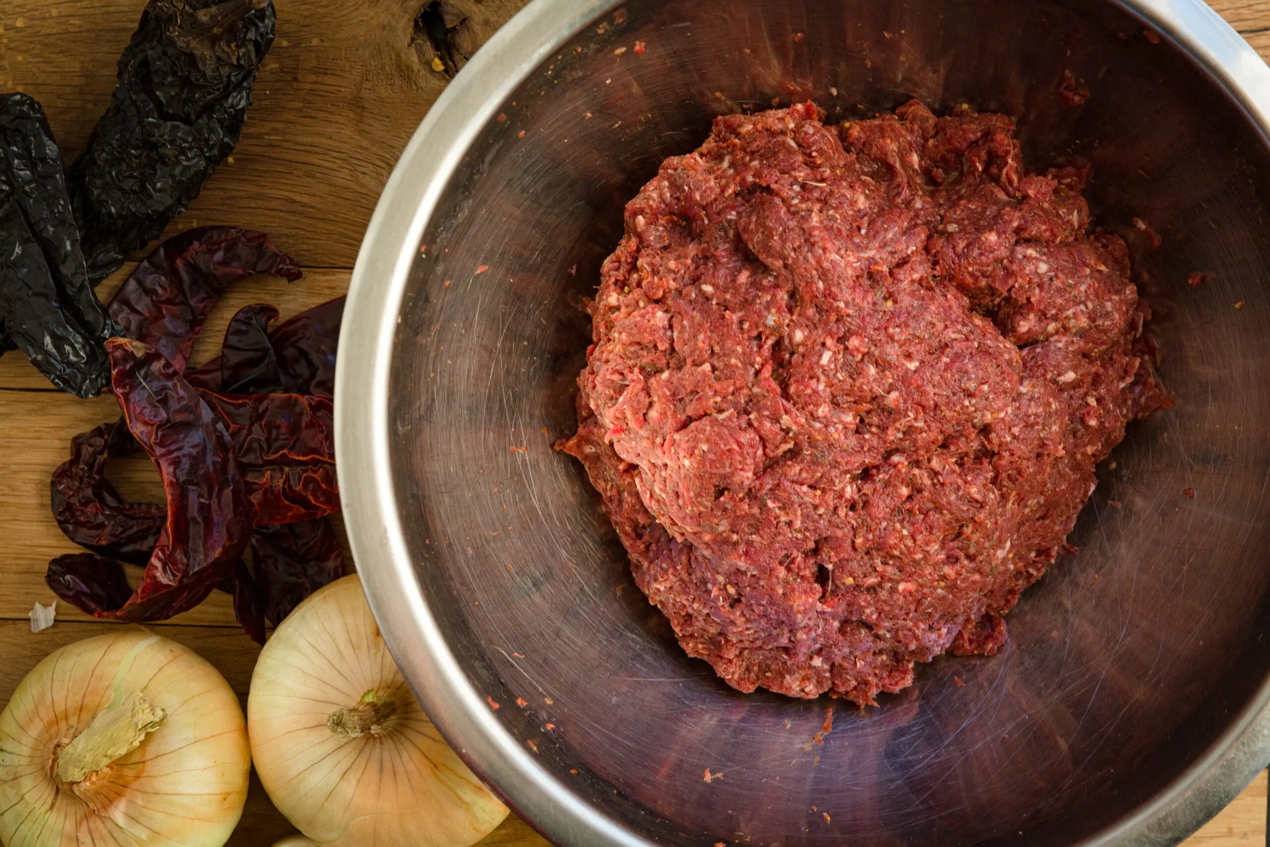 Raw ground venison in a metal bowl resting on a table.