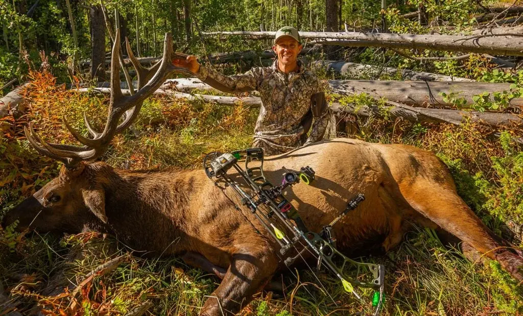 elk hunter kneeling behind giant elk