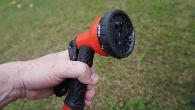 The red and black nozzle of a hydropod shower being held in front of a green grass background. 