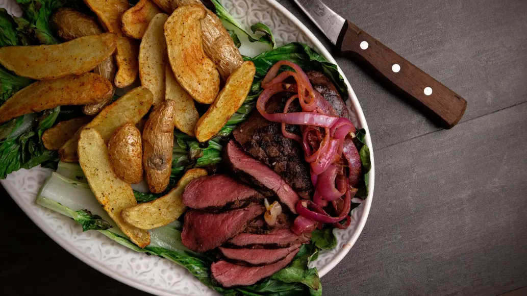 Plate of venison backstrap with potatoes and picked onions.