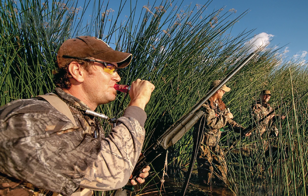 Three teal duck hunters sand agains reeds in a levee