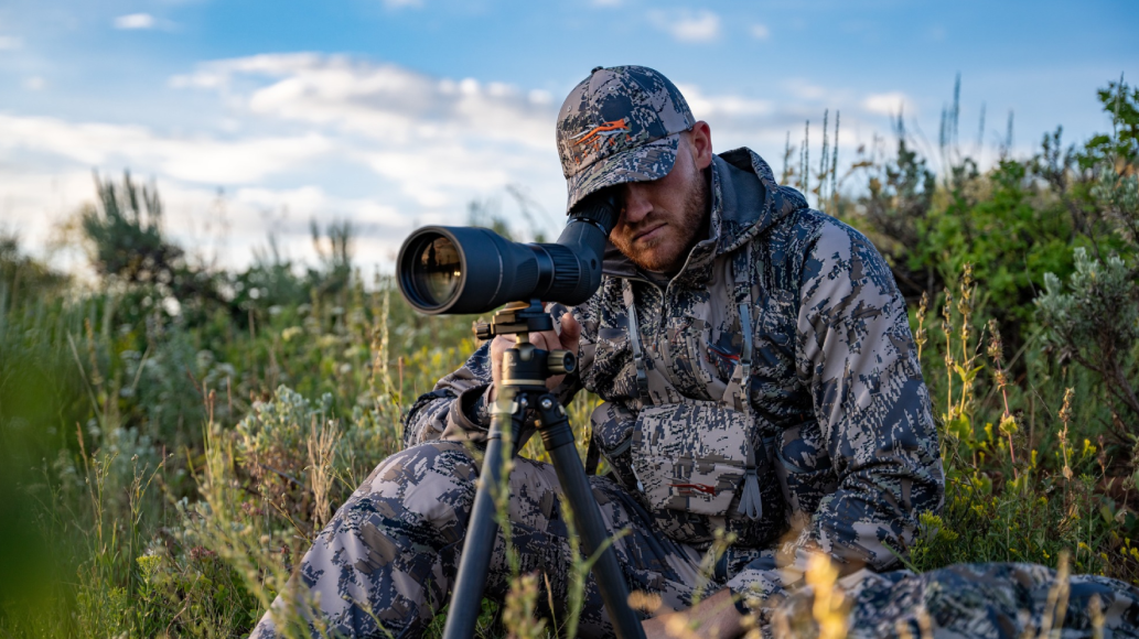 Hunter wearing Sitka gear looking through spotting scope