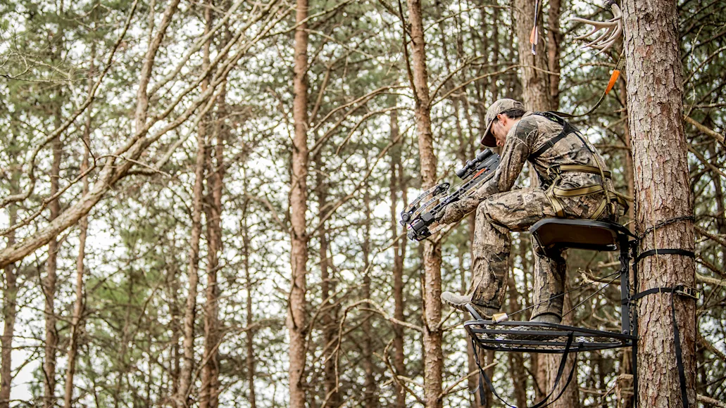 A man in a tree stand hunting with a crossbow.