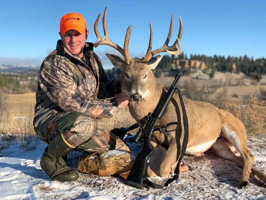 Hunter kneeling beside a deer in the snow.