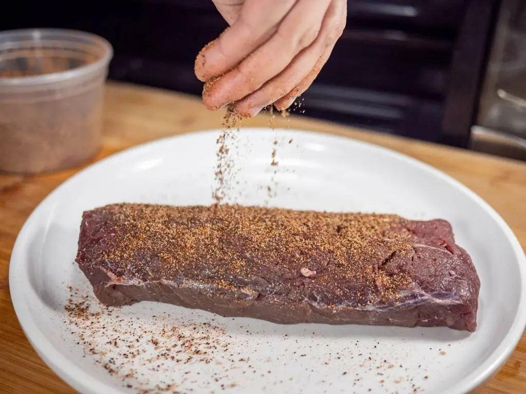 A dry rub being spread onto a venison backstrap.