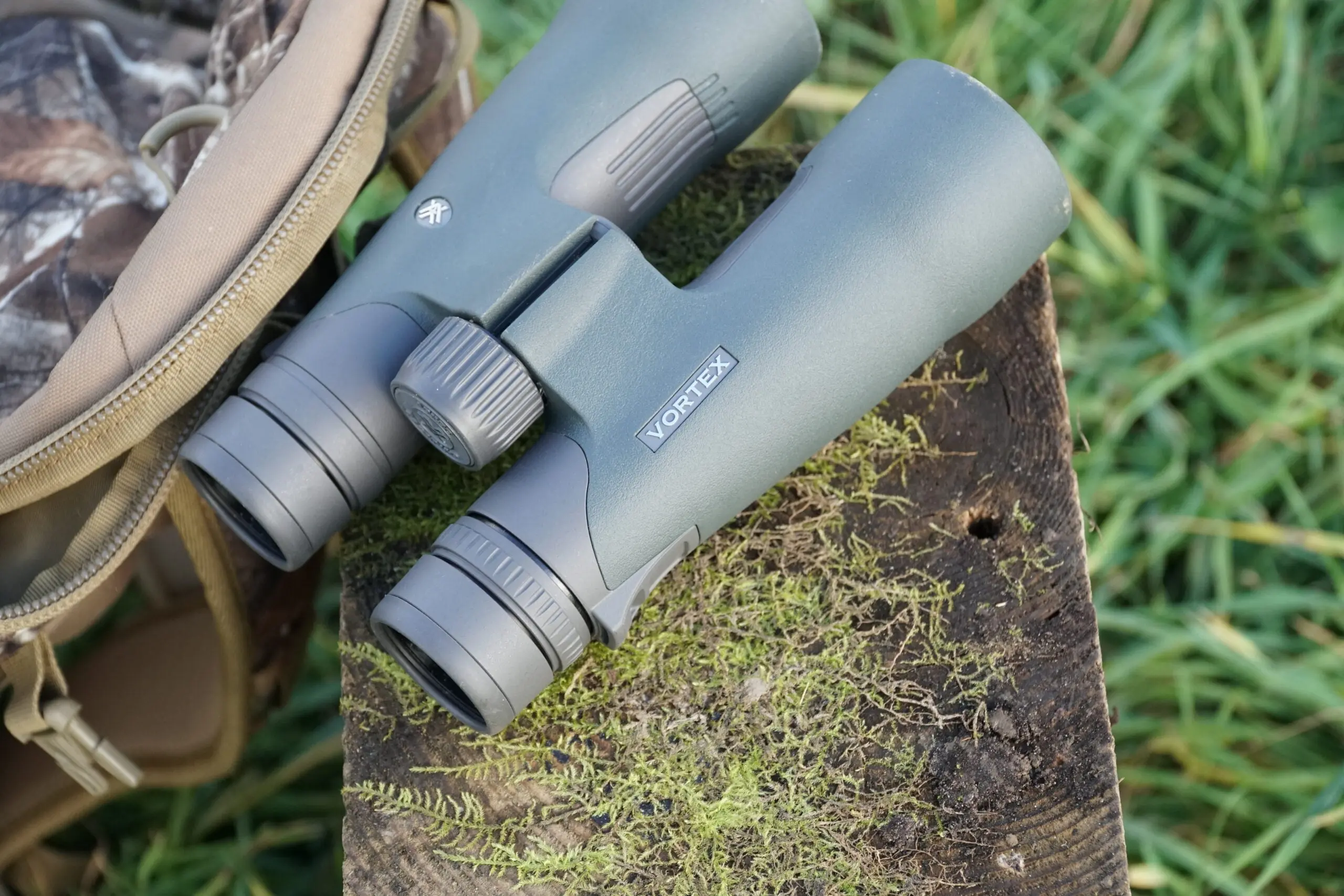 Vortex Razor UHD 10x50 binocular sitting on mossy block of wood with camo pack nearby