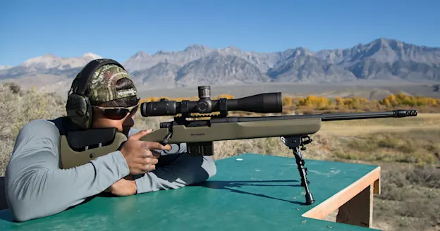 photo of a hunter shooting from a bench with a rifle that has a muzzle brake